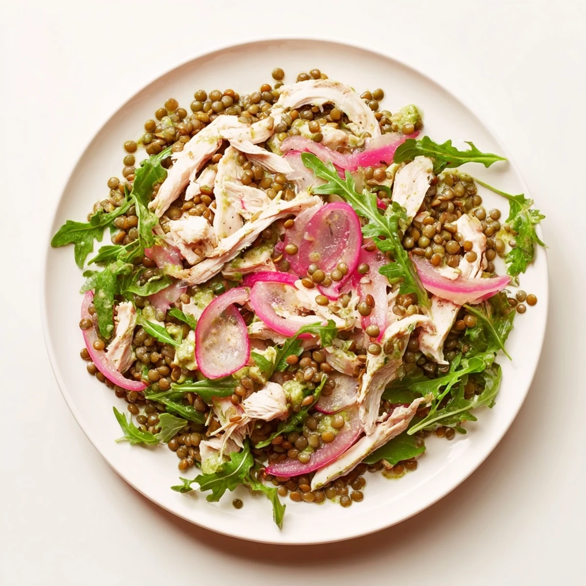 A close-up of Lentil & Chicken Spring Salad with glistening arugula, tender lentils, juicy chicken, and vibrant pickled onions.