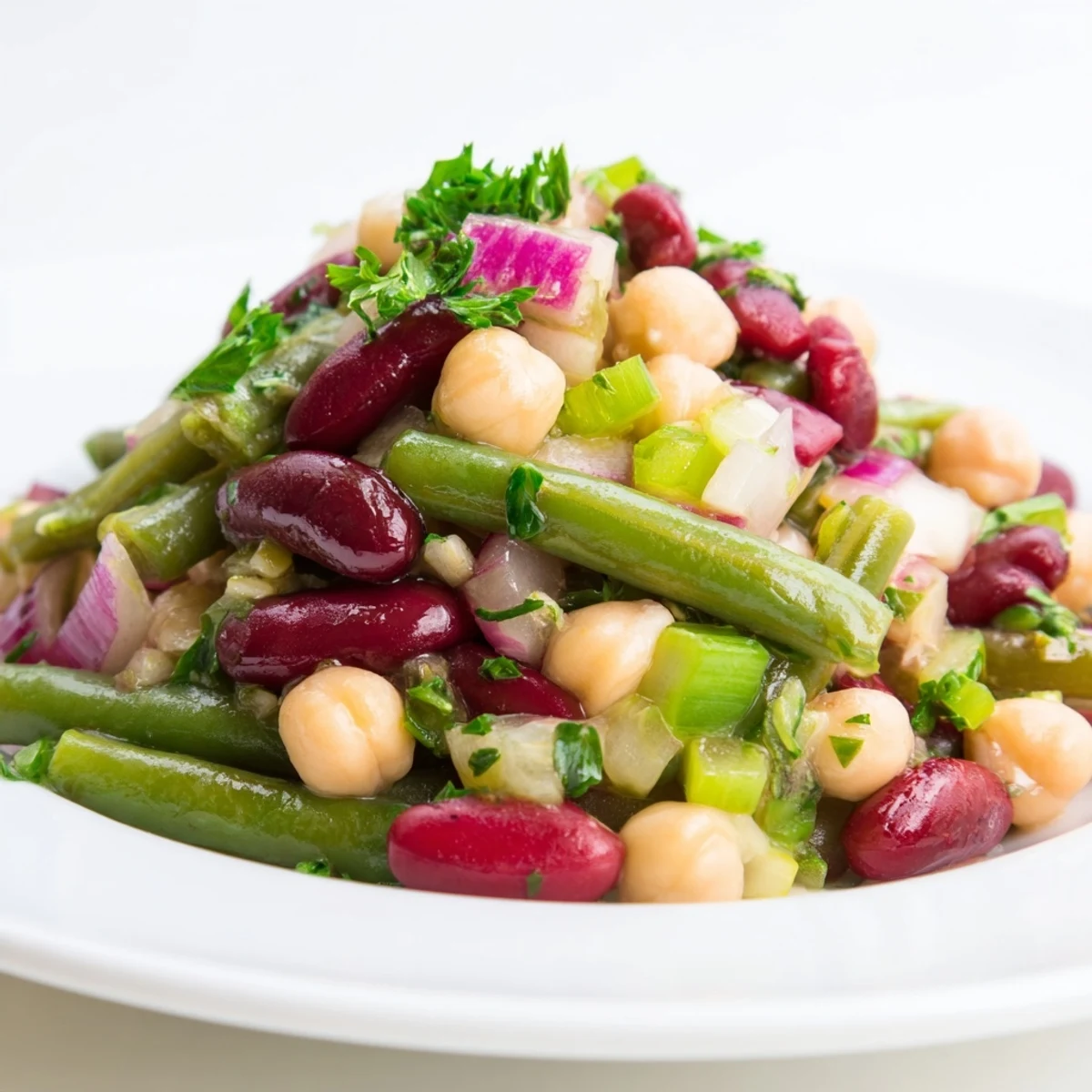 A vibrant bowl of Three-Bean Salad, featuring chickpeas, kidney beans, and crisp green beans tossed with fresh parsley and red onion.