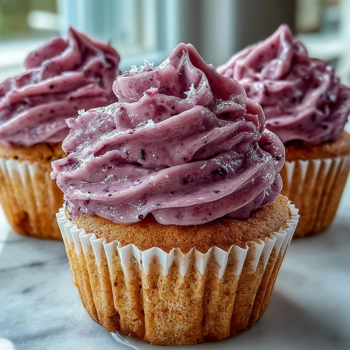Warm olive oil cupcakes with black currant frosting, arranged on a rustic cooling rack ready for afternoon tea.