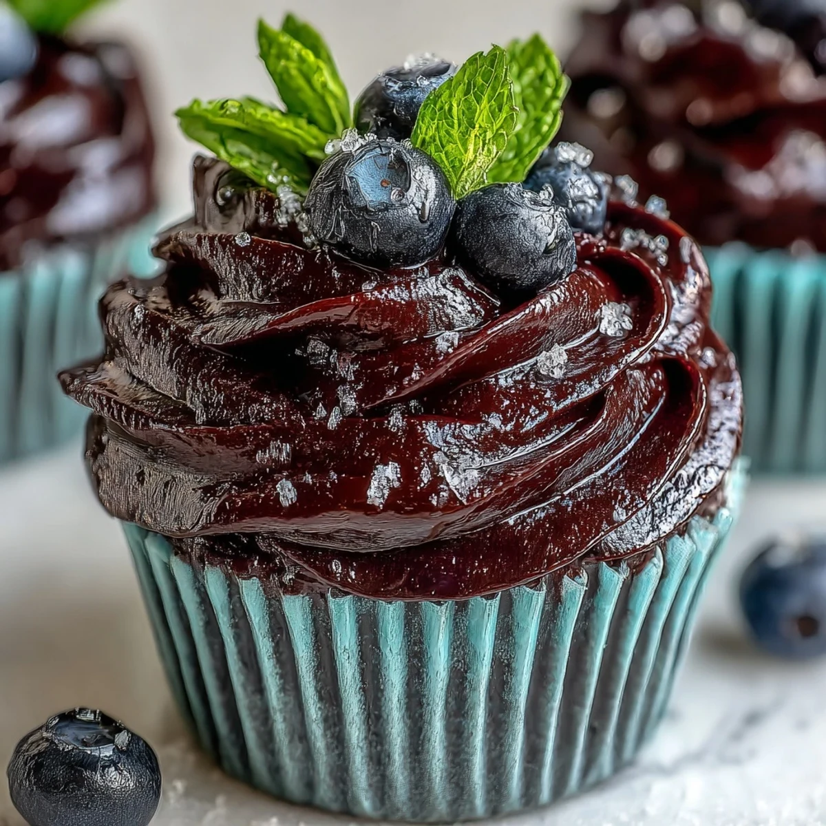 Fresh black currant garnish tops a vanilla cupcake with vibrant Black Currant Frosting.