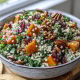 Orange-honey dressing glistens on tender pearl couscous and kale, dotted with crunchy pecans and cranberries in a festive serving bowl.