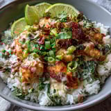 Spoonful of tender chicken coated in creamy coconut sauce lifted from a Coconut Chicken Rice Bowl, with fluffy jasmine rice and fresh herbs.