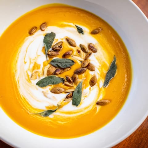 A bowl of savory, aromatic Butternut Squash Soup, garnished with toasted pumpkin seeds and sage.