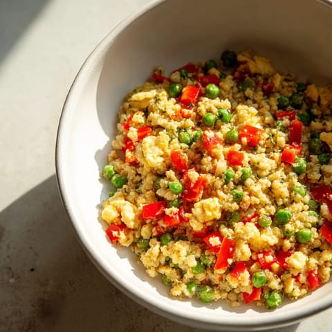 Vibrant Cauliflower Fried Rice with colorful peas, carrots, and sautéed garlic served hot in a white bowl.
