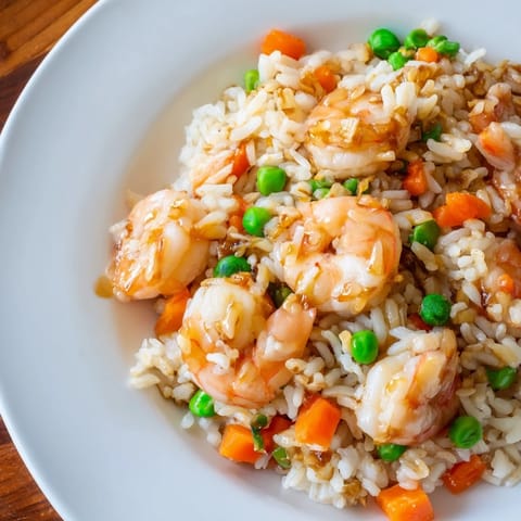 A close-up of vibrant Shrimp Garlic Fried Rice garnished with fresh green onions, showcasing tender pink shrimp nestled in aromatic, steaming grains.