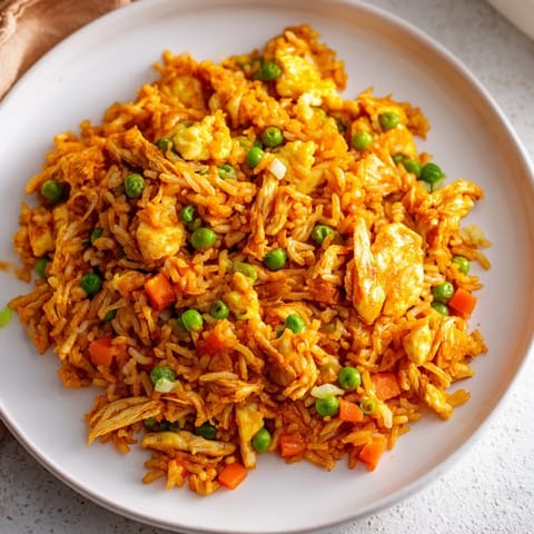 Golden-brown Butter Chicken Fried Rice with vibrant peas and carrots, garnished with fresh green onions.