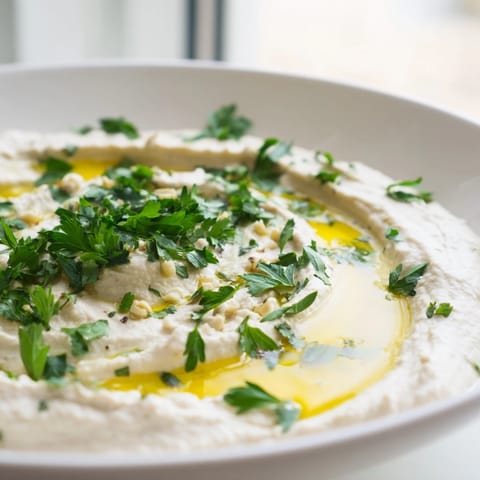 A vibrant bowl of White Bean Dip, garnished with parsley and lemon zest, perfect for parties or healthy snacking.  