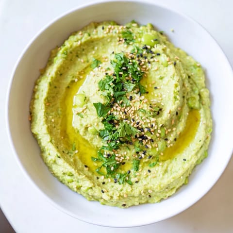 Creamy, vibrant Edamame Hummus blended with tahini and lemon, garnished with olive oil and toasted sesame seeds in a rustic bowl.  