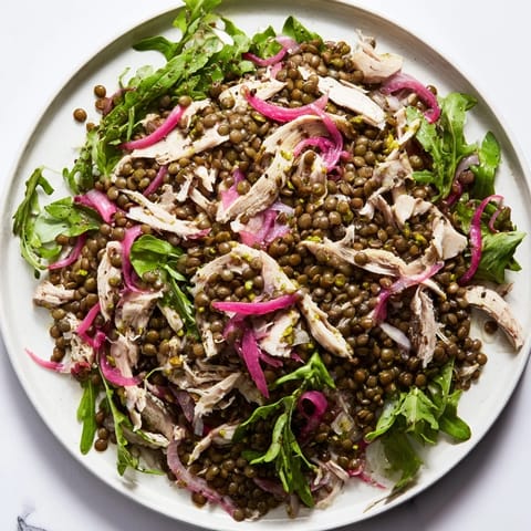 Lentil & Chicken Spring Salad plated beside a linen napkin, showcasing fresh cherry tomatoes, cucumber slices, and a drizzle of mustard dressing.