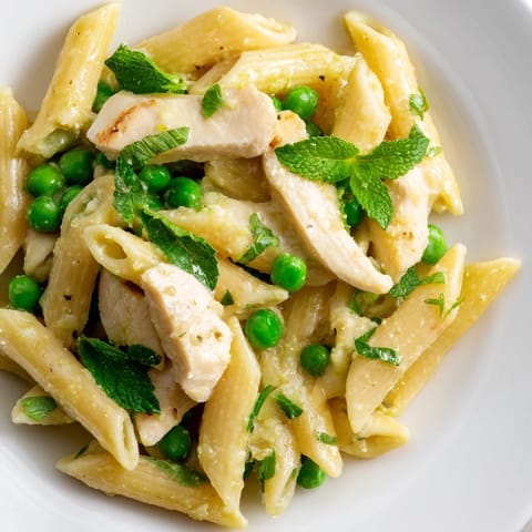 A plated serving of Pea & Mint Chicken Pasta topped with extra Parmesan, showcasing tender chicken and vibrant mint leaves.