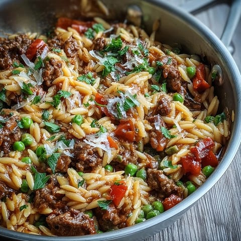 Ground Beef Orzo Dinner served in a skillet with vibrant red tomatoes, peas, and savory beef.