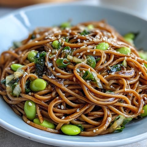Sesame Ginger Noodle Bowl with crunchy cabbage, carrots, and edamame, drizzled with zesty sesame ginger dressing for a refreshing meal.