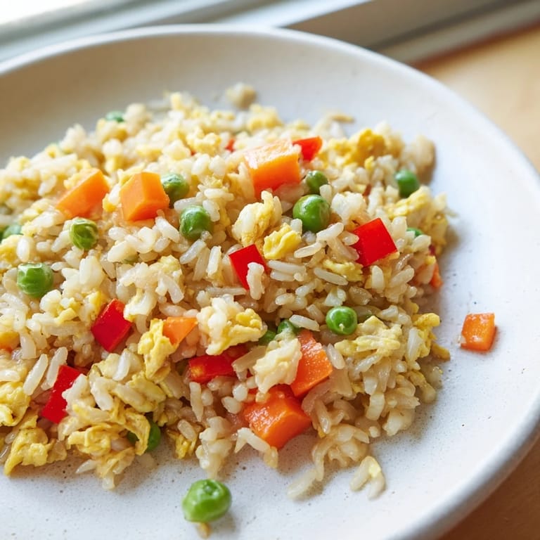 A close-up of Egg Fried Rice garnished with scallions, served steaming hot next to a small soy sauce drizzle.
