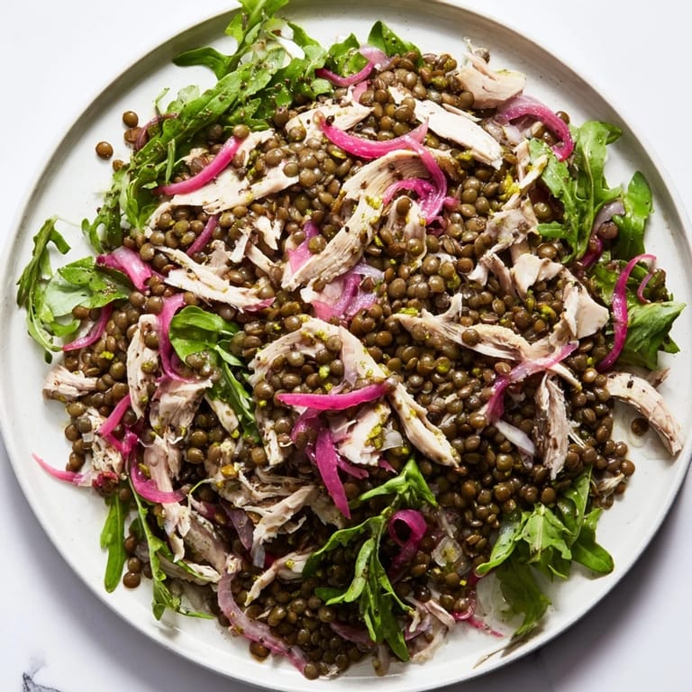 Lentil & Chicken Spring Salad plated beside a linen napkin, showcasing fresh cherry tomatoes, cucumber slices, and a drizzle of mustard dressing.