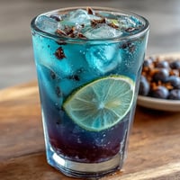 A vibrant glass of butterfly pea flower color-change lemonade, shifting from blue to purple as citrus mixes in, served over ice with lemon slices.