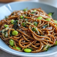 Sesame Ginger Noodle Bowl with crunchy cabbage, carrots, and edamame, drizzled with zesty sesame ginger dressing for a refreshing meal.